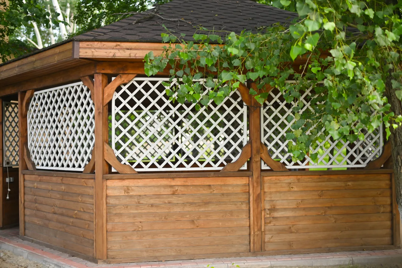 Drewniana altana z ażurowymi panelami, idealna do ogrodu. Dowiedz się, jak zabudować ściany altany ogrodowej, by stworzyć przytulne miejsce.