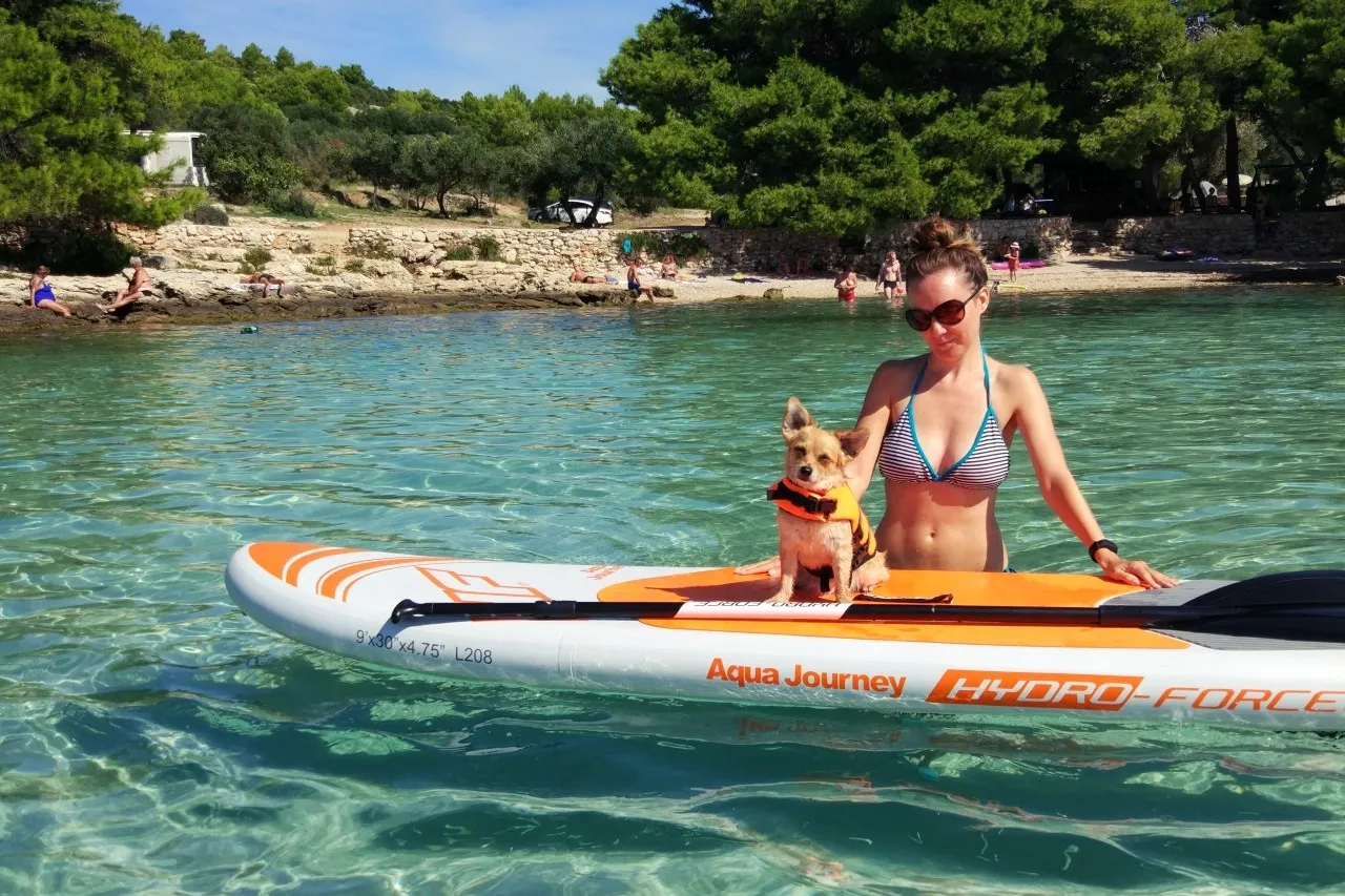 Chorwacja z psem na desce SUP. Mały piesek w kamizelce ratunkowej i jego pani cieszą się krystalicznie czystą wodą.