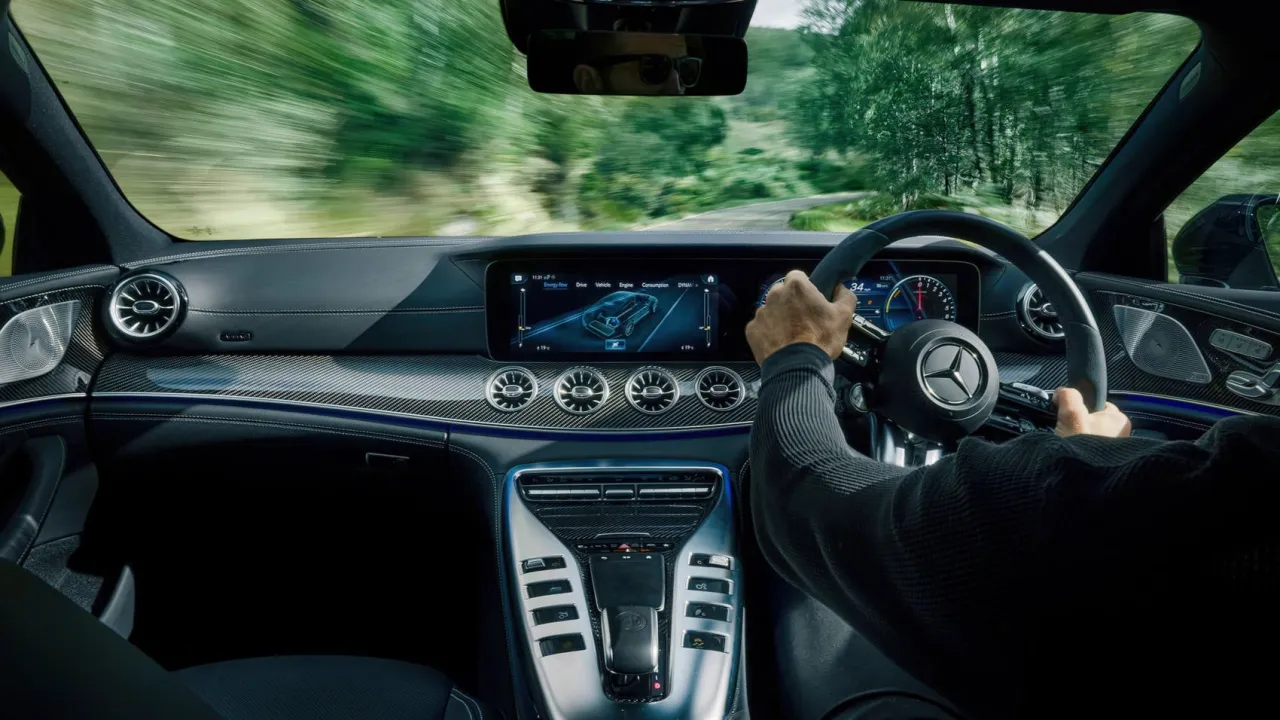 Wnętrze Mercedes-AMG GT 63 S z widokiem na drogę. Kierowca trzyma kierownicę, a na ekranie widnieje schemat samochodu.