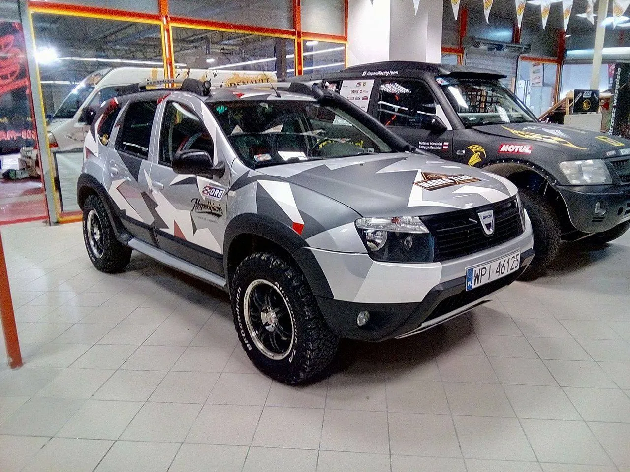 Dacia Duster z terenowym oklejeniem, idealne jakie auto na ryby. Obok czarny Jeep.