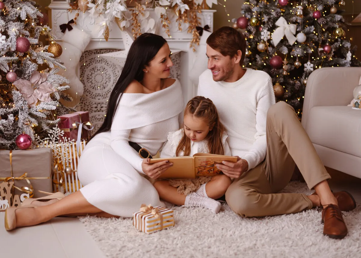 Rodzina w białych strojach czyta książkę przy choince. Idealny pomysł, jak się ubrać na święta bożego narodzenia.