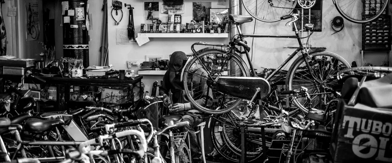 Warsztat rowerowy, gdzie mechanik przygotowuje rower do sezonu. W tle p&oacute;łki z częściami i narzędziami.