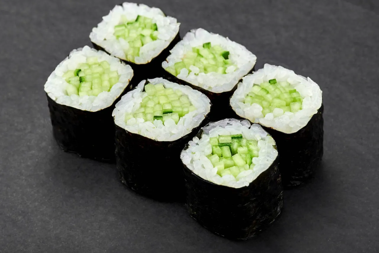 Sześć kawałków sushi z ogórkiem, z ryżem i nori, ułożonych na ciemnym tle.