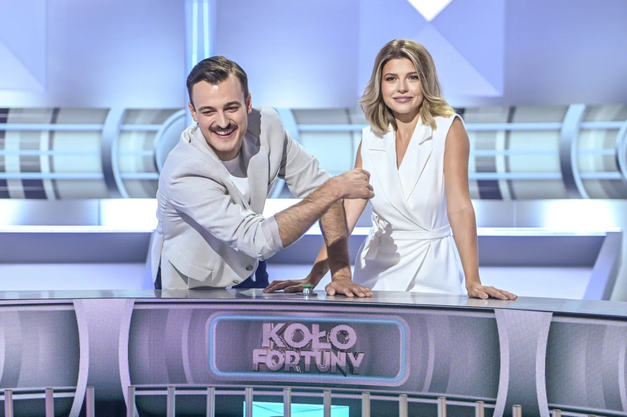 Uśmiechnięty prowadzący i jego koleżanka przy pulpicie 