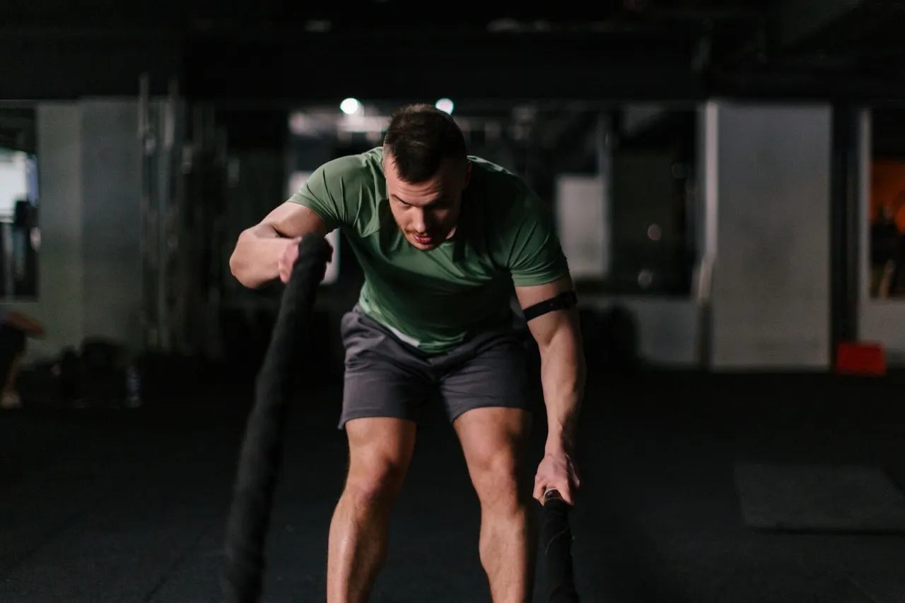 Intensywny trening z linami to świetny sposób, jak przyspieszyć spalanie tłuszczu. Mężczyzna w zielonej koszulce ćwiczy w siłowni.
