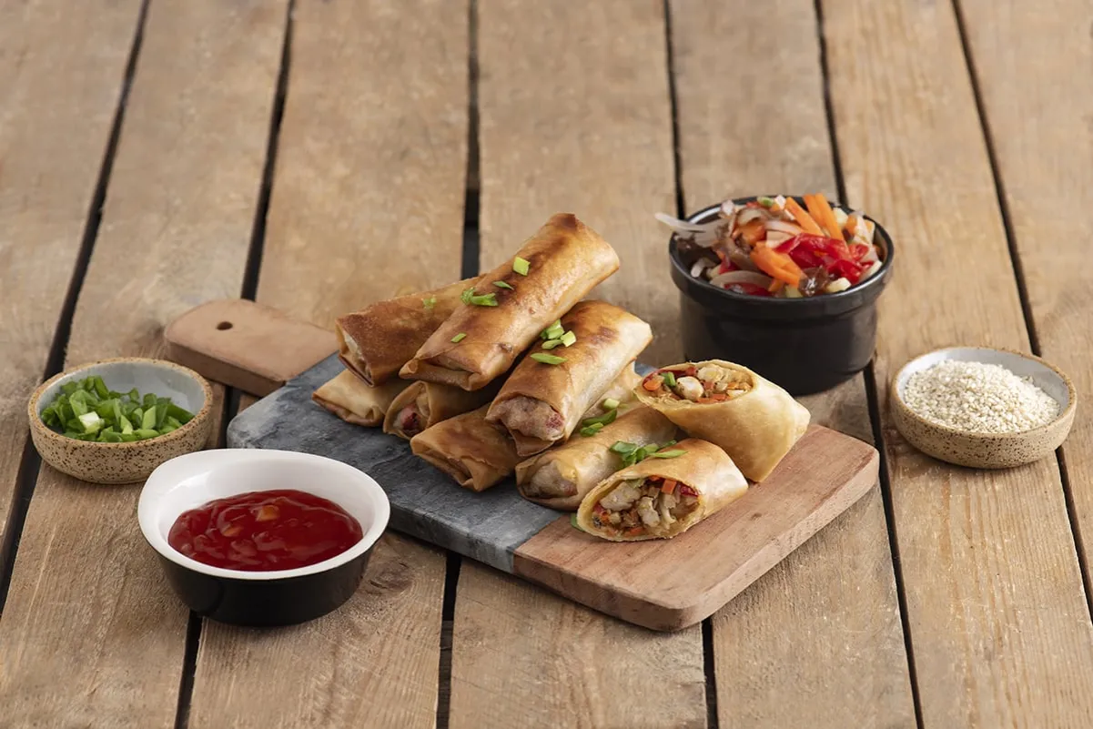 Chrupiące sajgonki z kurczakiem, podane z sosem, warzywami i sezamem. Idealna przekąska na każdą okazję.