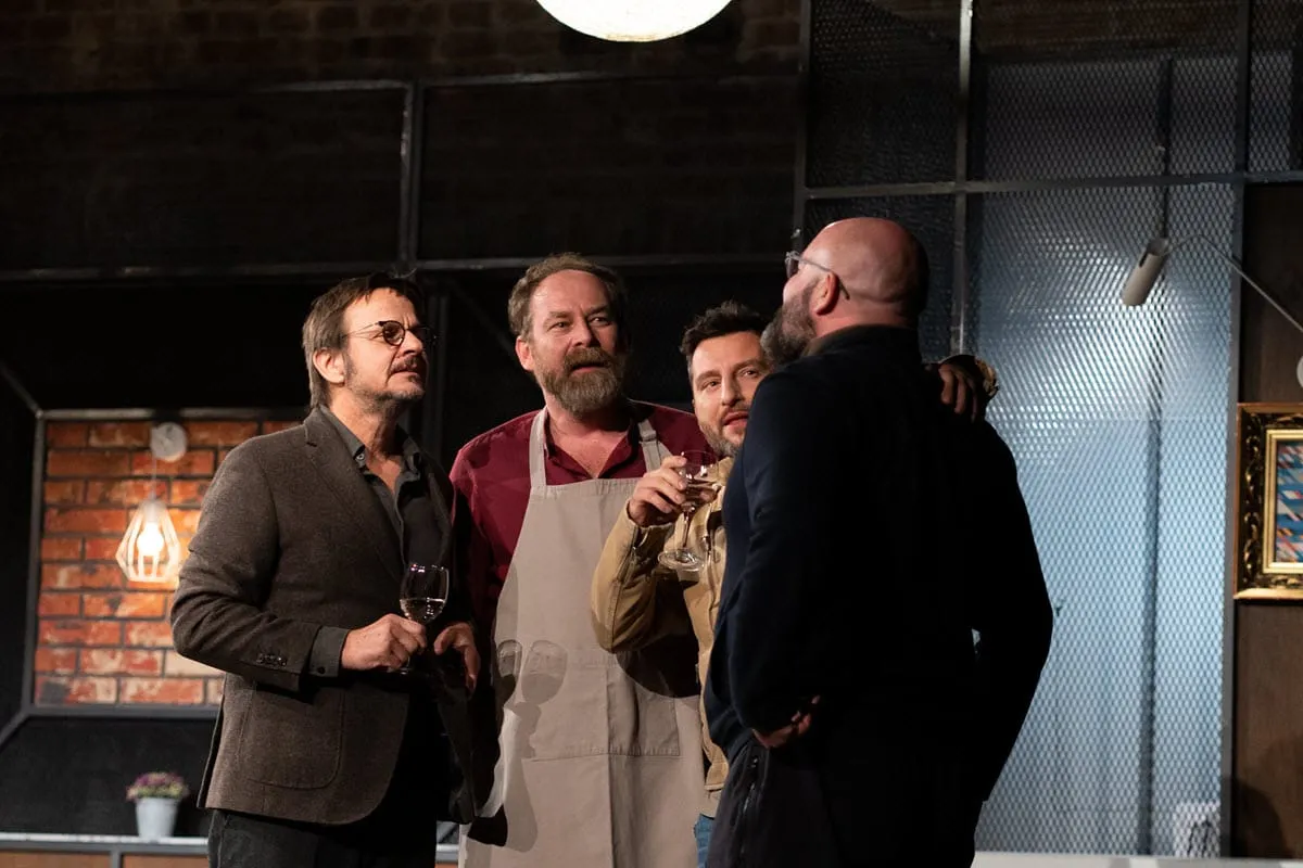 Czterech mężczyzn rozmawia przy kieliszkach wina na scenie. Spektakl 