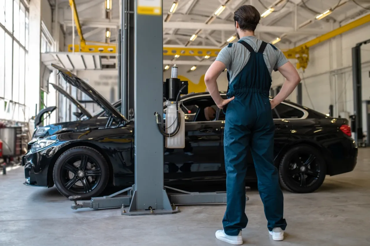 Mechanik w warsztacie samochodowym, zastanawia się, ile zarabia kierowca mechanik. Dwa czarne auta na podnośniku.