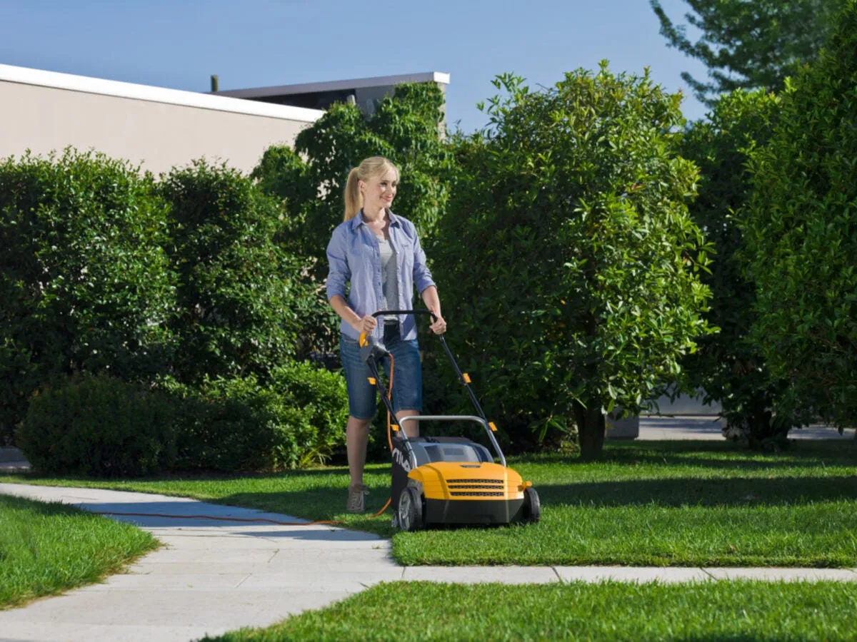Kobieta z kosiarką elektryczną na trawniku. To skuteczny spos&oacute;b, jak pozbyć się mchu z trawnika i cieszyć się zieloną murawą.