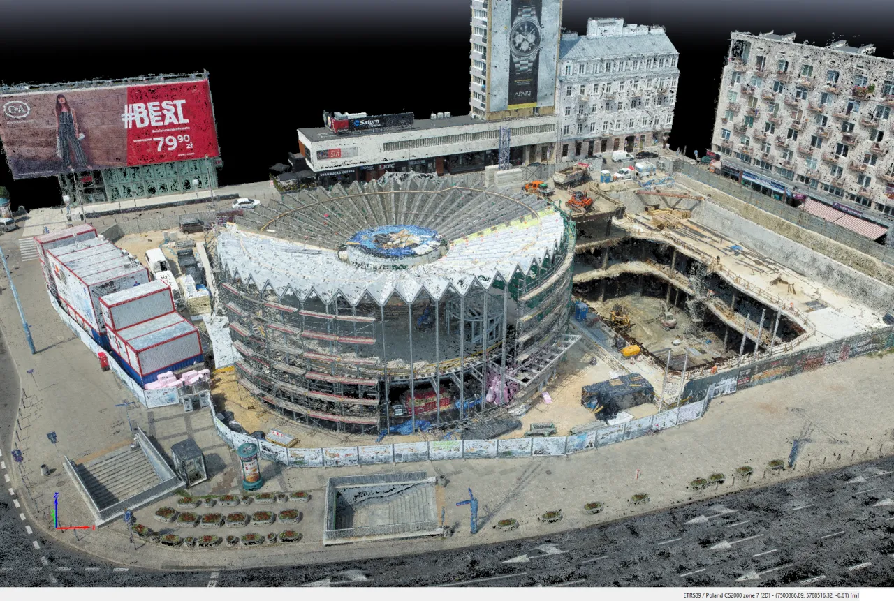 Geodeta dokumentuje postęp prac na budowie. Widoczny jest nowoczesny budynek w budowie, otoczony rusztowaniami i placem budowy z maszynami.