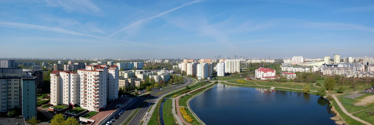 Widok na jezioro i osiedla mieszkaniowe w dzielnicy Gocław w Warszawie. W tle widać panoramę miasta.