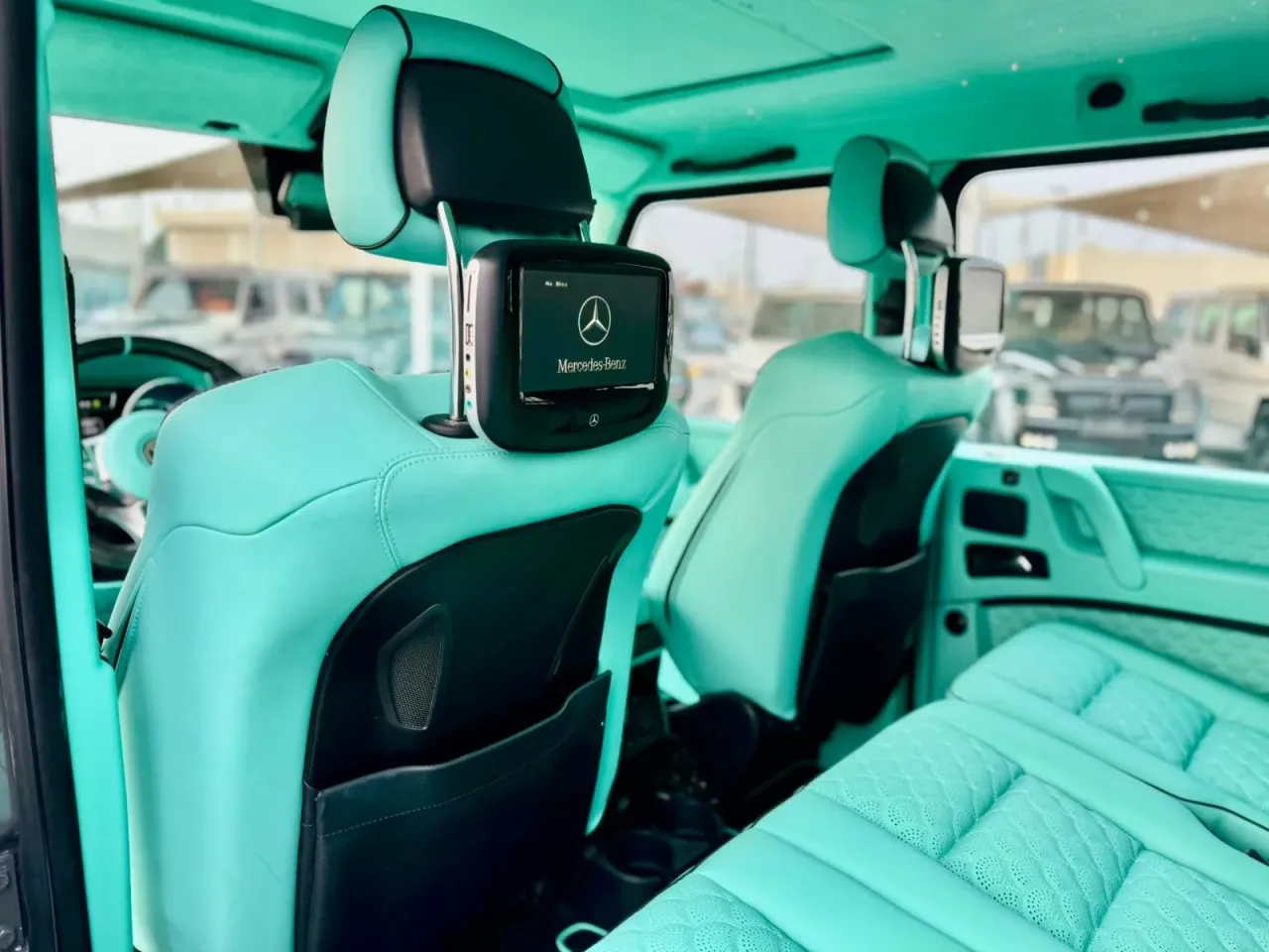 Wnętrze Mercedes G Klasa AMG w turkusowej skórze. Widoczne ekrany multimedialne w zagłówkach.