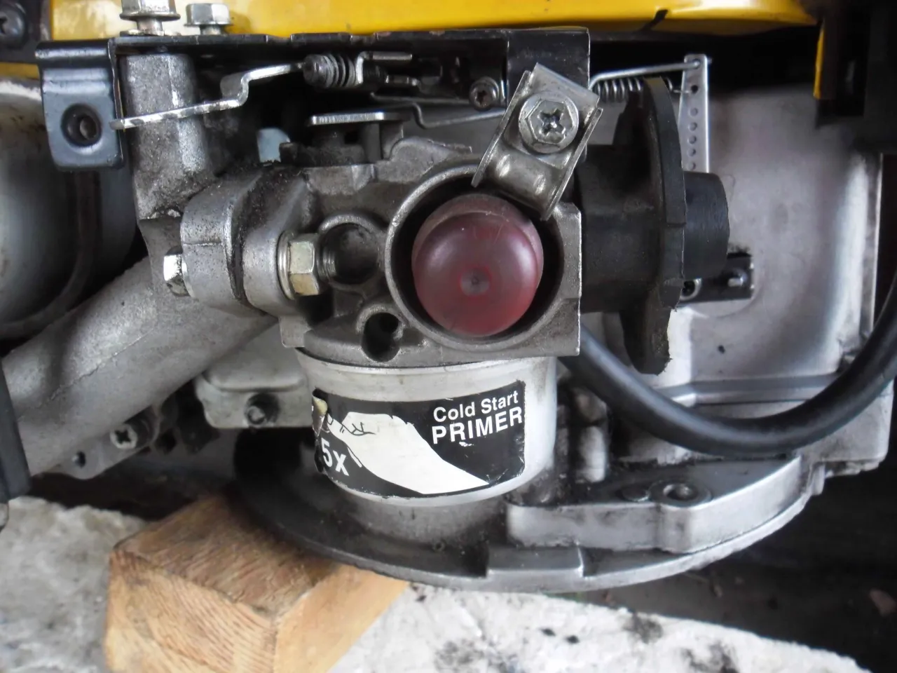 Zbliżenie na gaźnik kosiarki spalinowej z czerwonym przyciskiem 