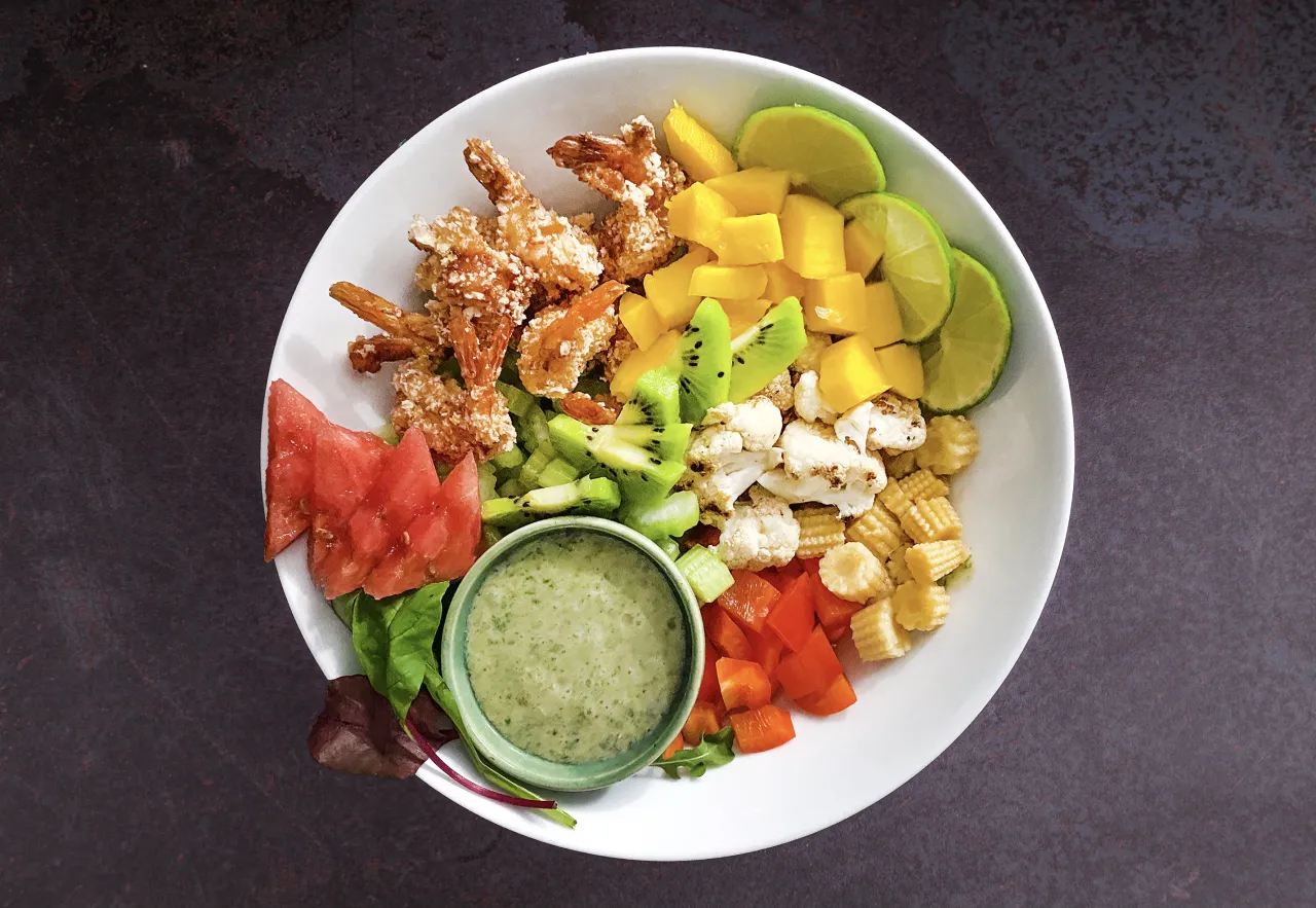 Kolorowy bowl z krewetkami w panierce, mango, kiwi, kalafiorem, kukurydzą, papryką, arbuzem i zielonym sosem.