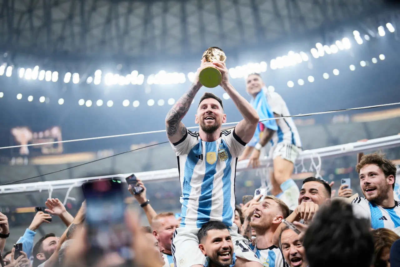 Leo Messi, kto jest mistrzem świata w piłce nożnej, triumfalnie unosi Puchar Świata, niesiony na ramionach przez kolegów z drużyny Argentyny.