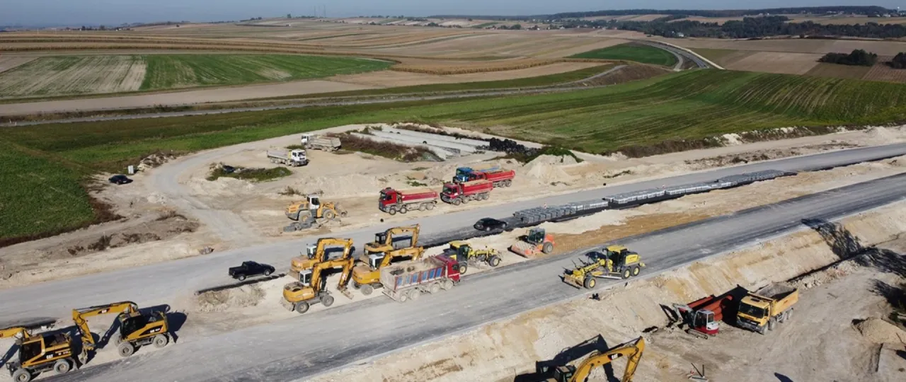 Budowa drogi ekspresowej na trasie Krak&oacute;w-Miech&oacute;w. Ciężki sprzęt budowlany pracuje na placu budowy, przygotowując nową trasę.