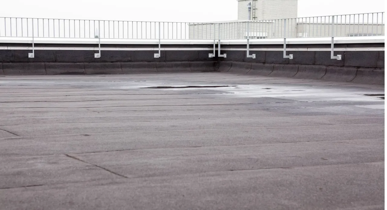 Płaski dach pokryty papą, z widocznymi śladami wilgoci i poręczą. Dowiedz się, jak naprawić dach pokryty papą, by zapobiec przeciekom.