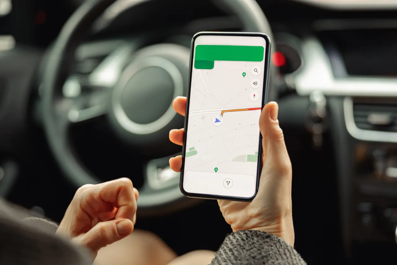 Kierowca trzyma telefon z nawigacją, rozmawiając przez niego. Czyżby dostał mandat za rozmowę przez telefon w trakcie jazdy?