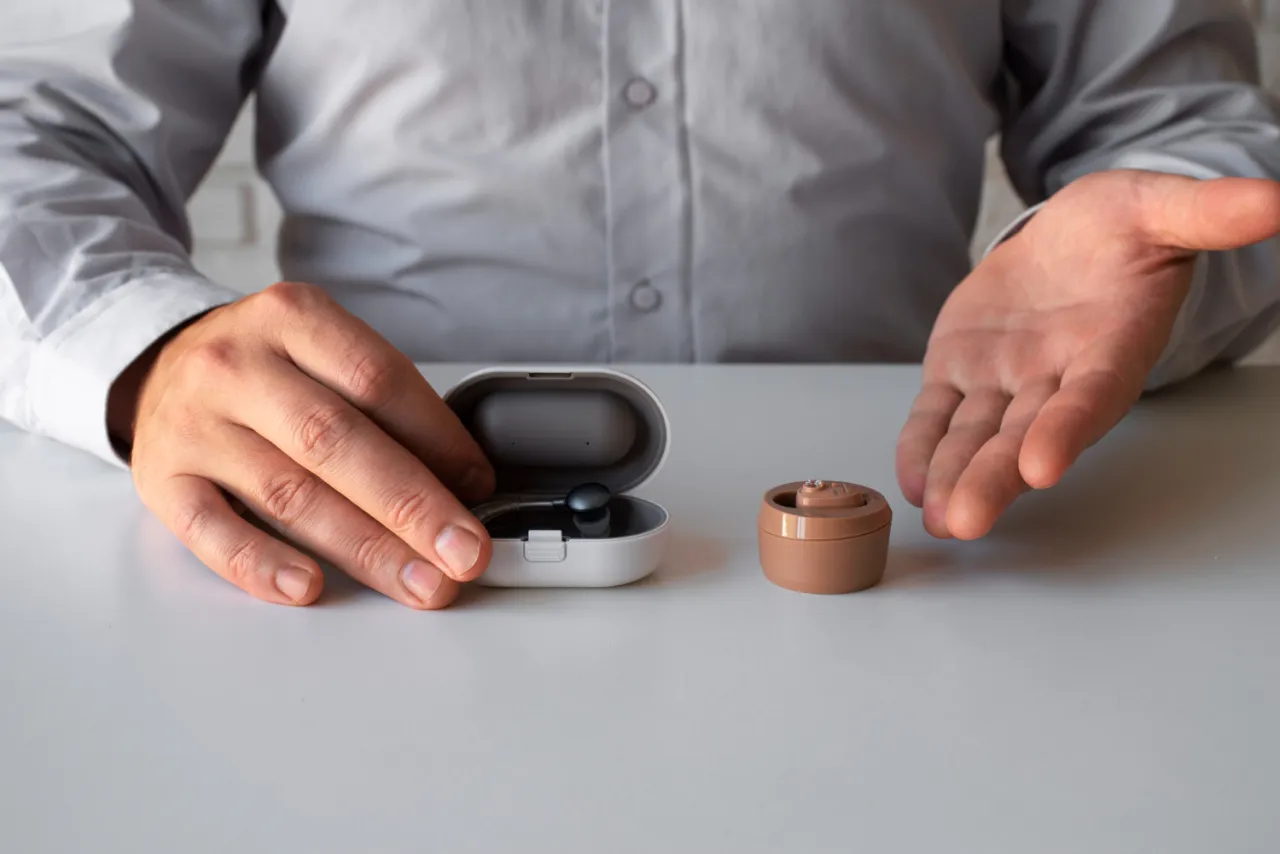 Dłonie mężczyzny prezentują aparaty słuchowe, jeden w etui. Zastanawiasz się, dlaczego aparat słuchowy szumi?