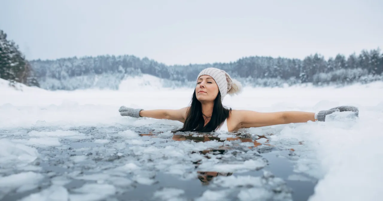 Kobieta w czapce i rękawiczkach zanurza się w lodowatej wodzie, doświadczając orzeźwiającego suchego morsowania.