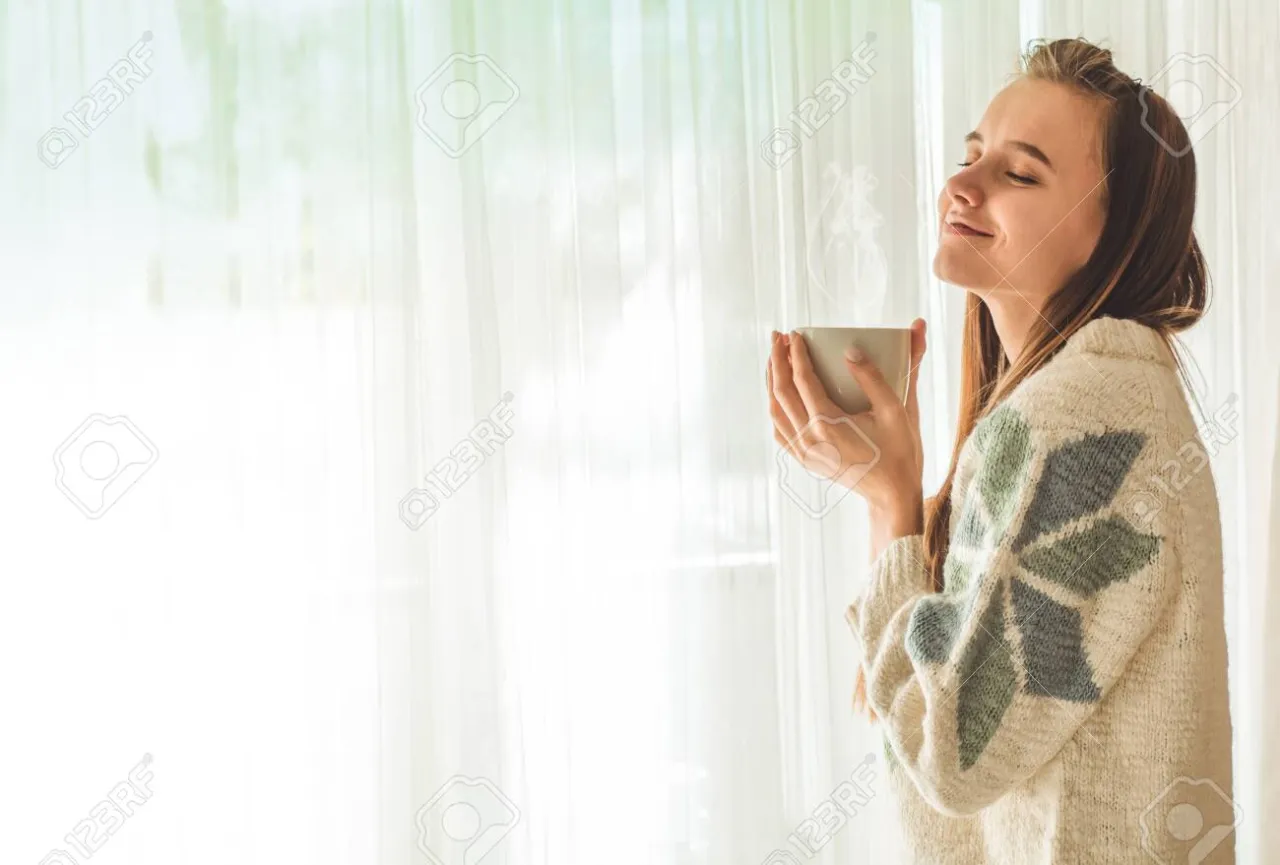 osoba medytująca przy oknie z filiżanką herbaty
