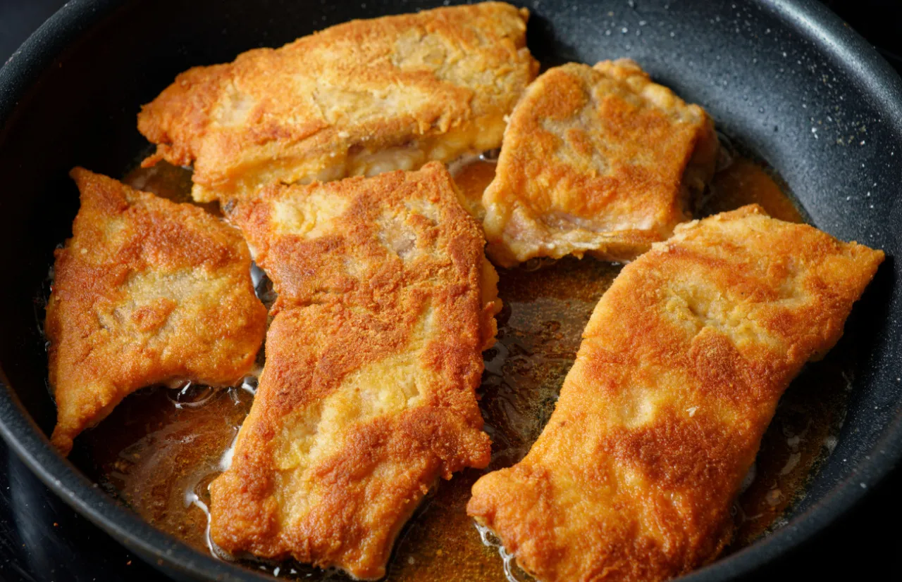 Smażone kawałki ryby w złocistej panierce bulgoczą na patelni. Idealne na obiad, gdy zastanawiasz się, na czym smażyć rybę w panierce.