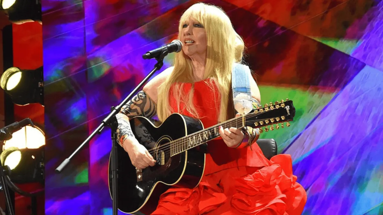 Maryla Rodowicz w czerwonej sukni gra na gitarze. Jej koncert trwa, a publiczność bawi się świetnie.