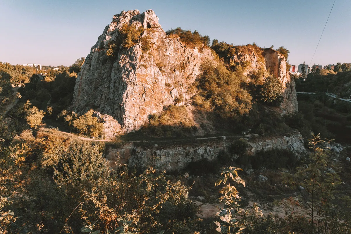 Skały i zieleń w rezerwat przyrody Kadzielnia. W oddali widać budynki.
