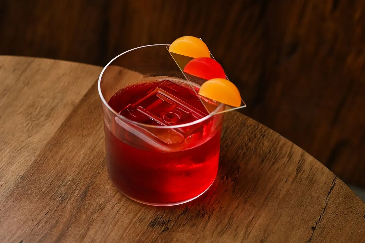 Klasyczny Negroni przepis: czerwony koktajl z lodem i pomarańczową dekoracją na szkle. Idealny na wieczór.