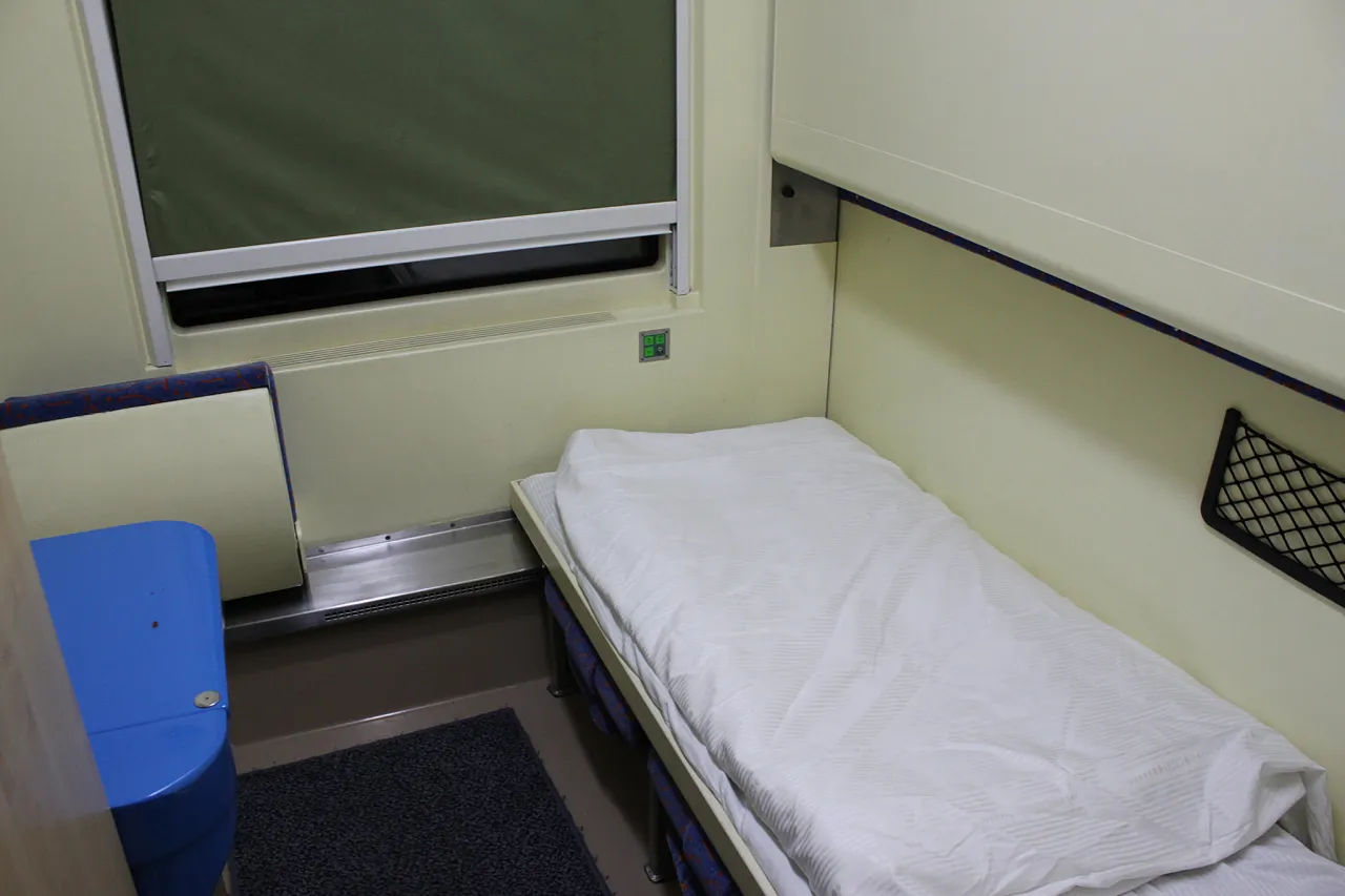 Wnętrze wagonu sypialnego z łóżkiem, oknem i niebieskim sedesem. Zastanawiasz się, ile kosztuje wagon sypialny?