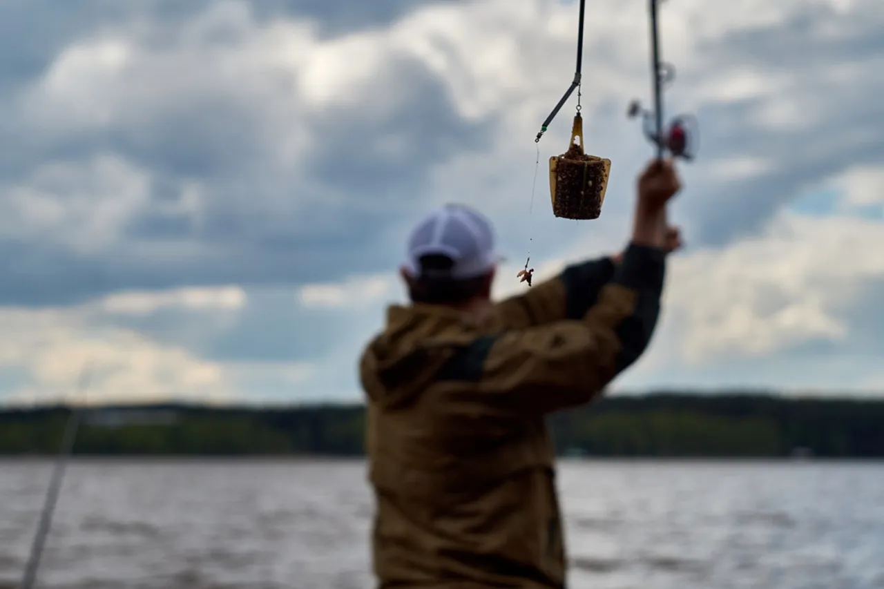 Wędkarz z koszyczkiem zanętowym na feederze, gotowy do zarzucenia.