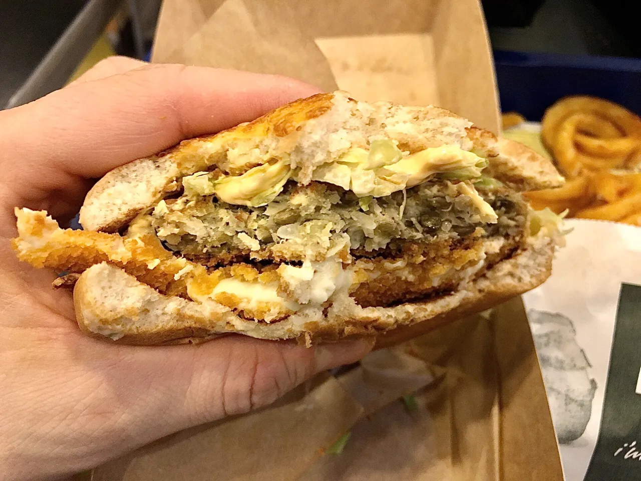 Wgryziony burger z Burger Kinga kontra obiad z restauracji. W ręce trzymam połówkę burgera z chrupiącym kotletem i sosem.