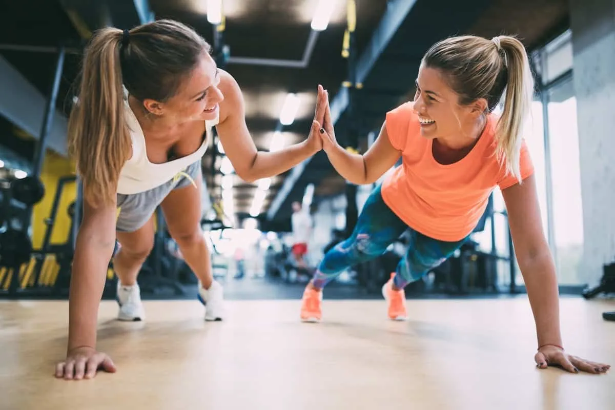 Dwie kobiety w siłowni robią pompki i dają sobie piątkę. Chcesz wiedzieć, jak zdobyć kartę multisport?
