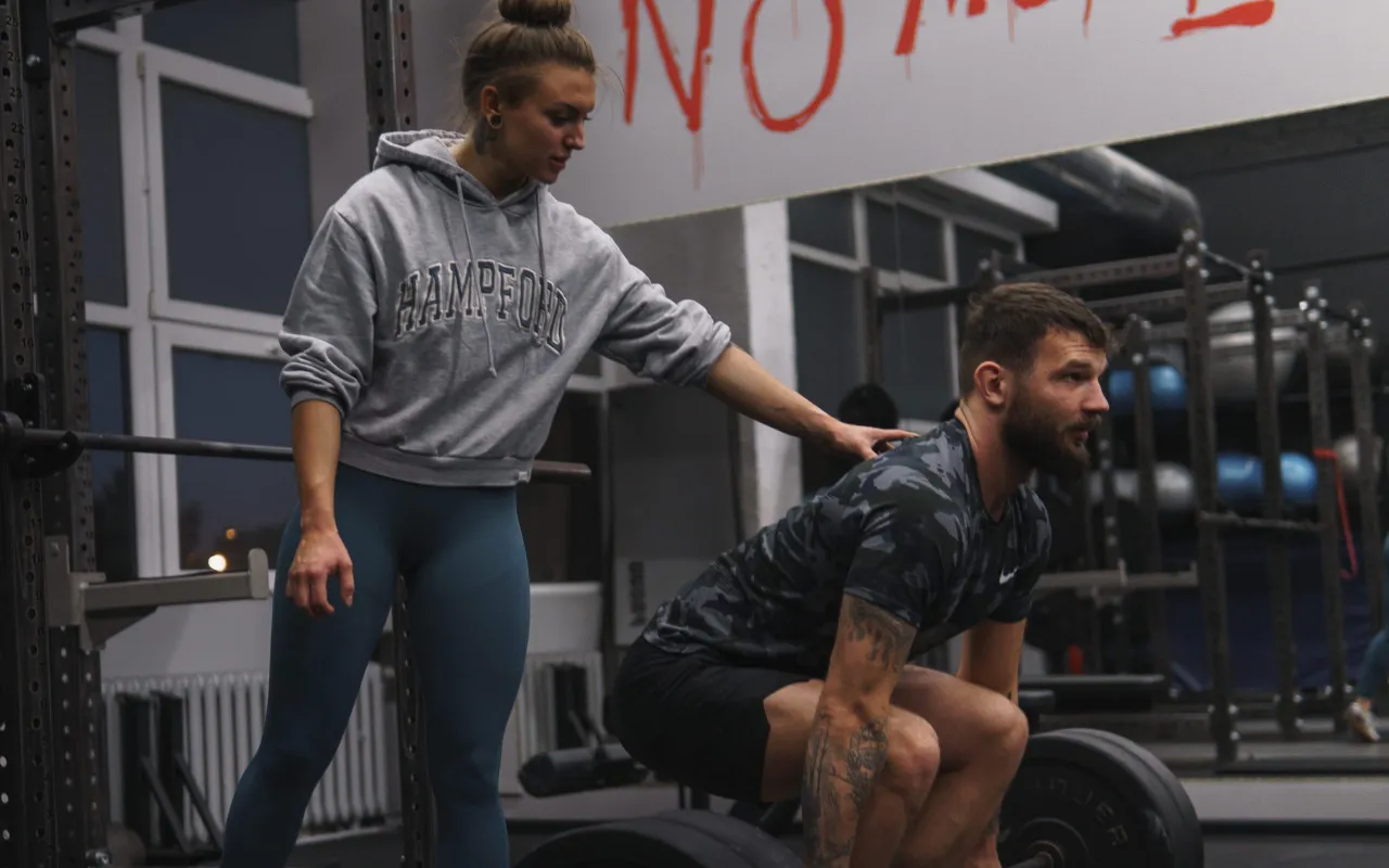 osoba początkująca na siłowni, instruktor pomaga