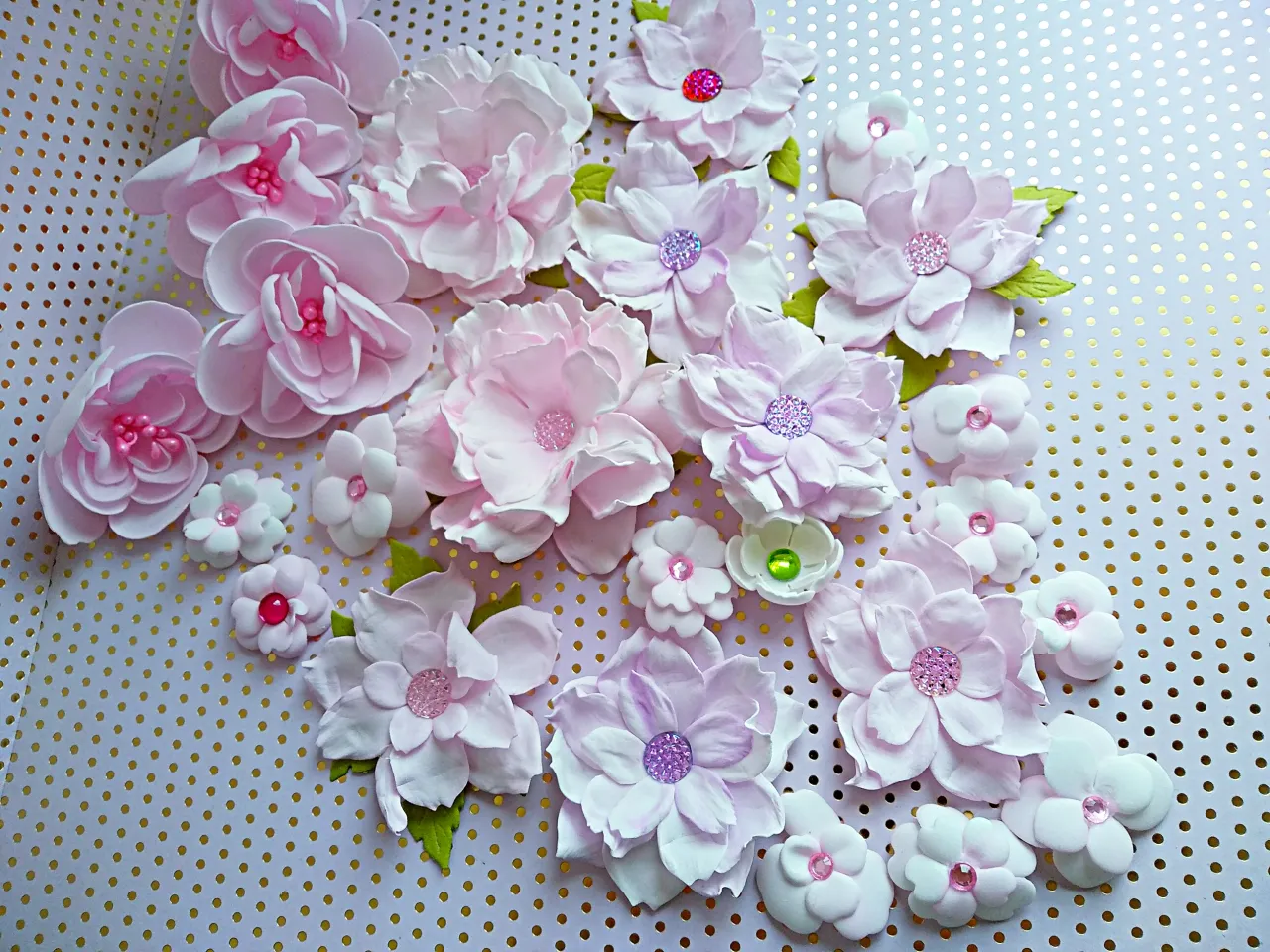 Kwiaty z pianki dekoracyjnej jak zrobić: różowe i fioletowe kwiaty z pianki z błyszczącymi środkami, ułożone na tle w złote kropki.