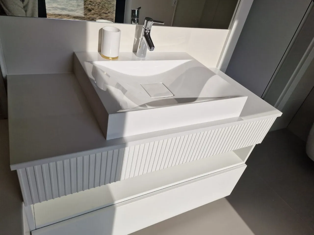 Nowoczesna łazienka z białym, prostokątnym umywalką nablatową. Blat łazienkowy z konglomeratu tworzy jednolitą, elegancką powierzchnię.