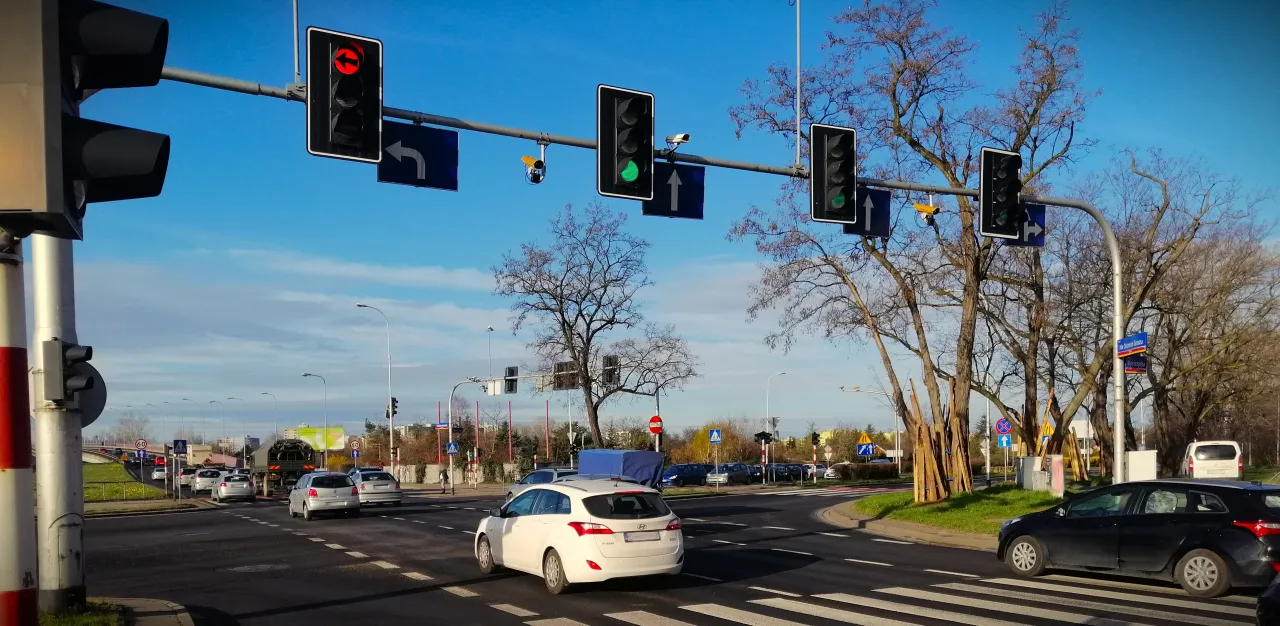Na skrzyżowaniu z sygnalizacją świetlną i fotoradarem, samochody czekają na zielone światło.