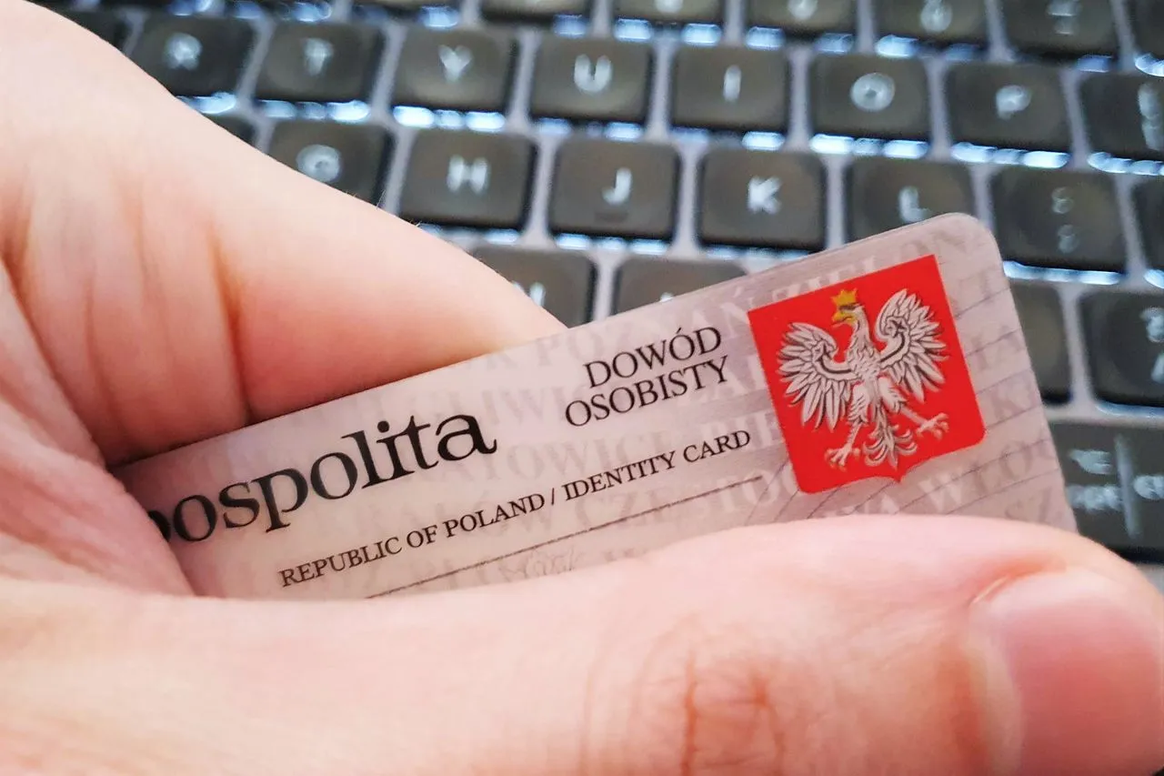 Dłoń trzyma dow&oacute;d osobisty na tle klawiatury. Chroń swoje dane, by jak uniemożliwić wzięcie pożyczki na nie.