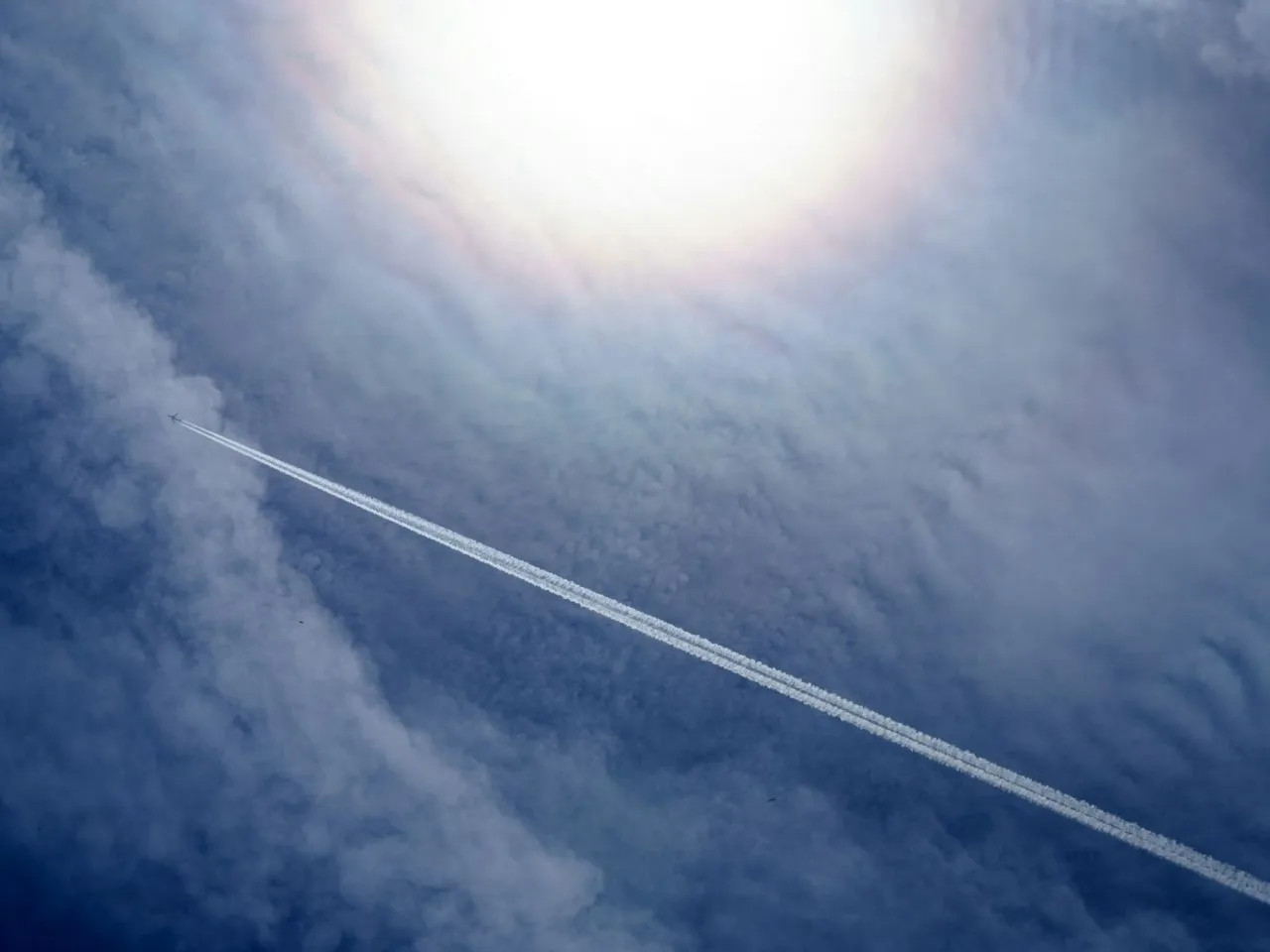 Samolot zostawia smugę na tle błękitnego nieba z chmurami. Zastanawiasz się, ile trwa lot z Polski na Teneryfę?