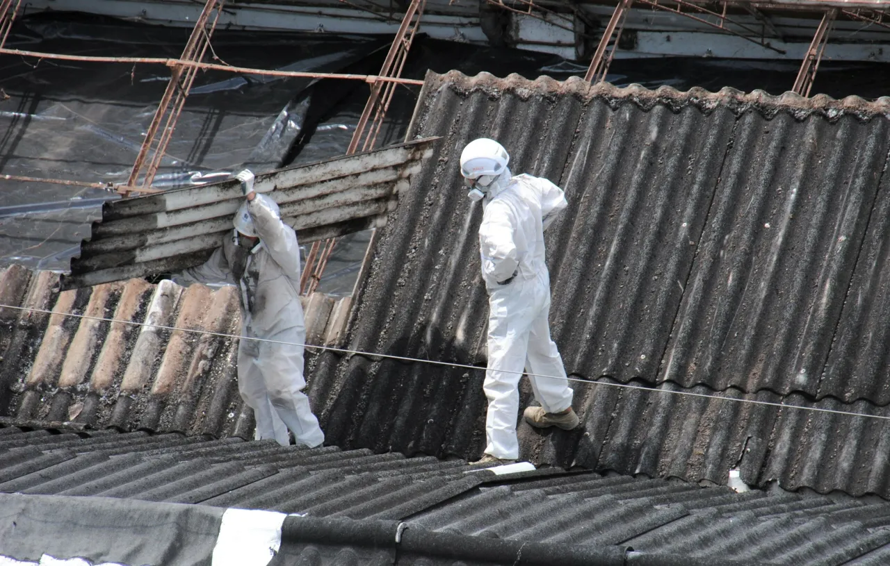 Pracownicy w kombinezonach ochronnych usuwają eternit z dachu. Dowiedz się, ile kosztuje usunięcie azbestu z dachu.