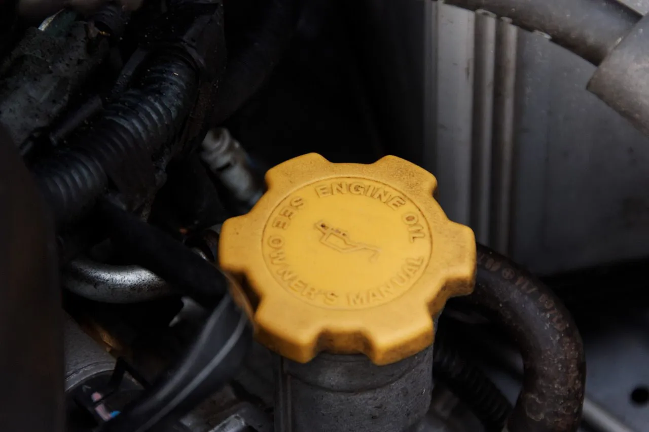 Pod maską samochodu 96: żółta zakrętka od oleju silnikowego, przewody i inne elementy silnika.