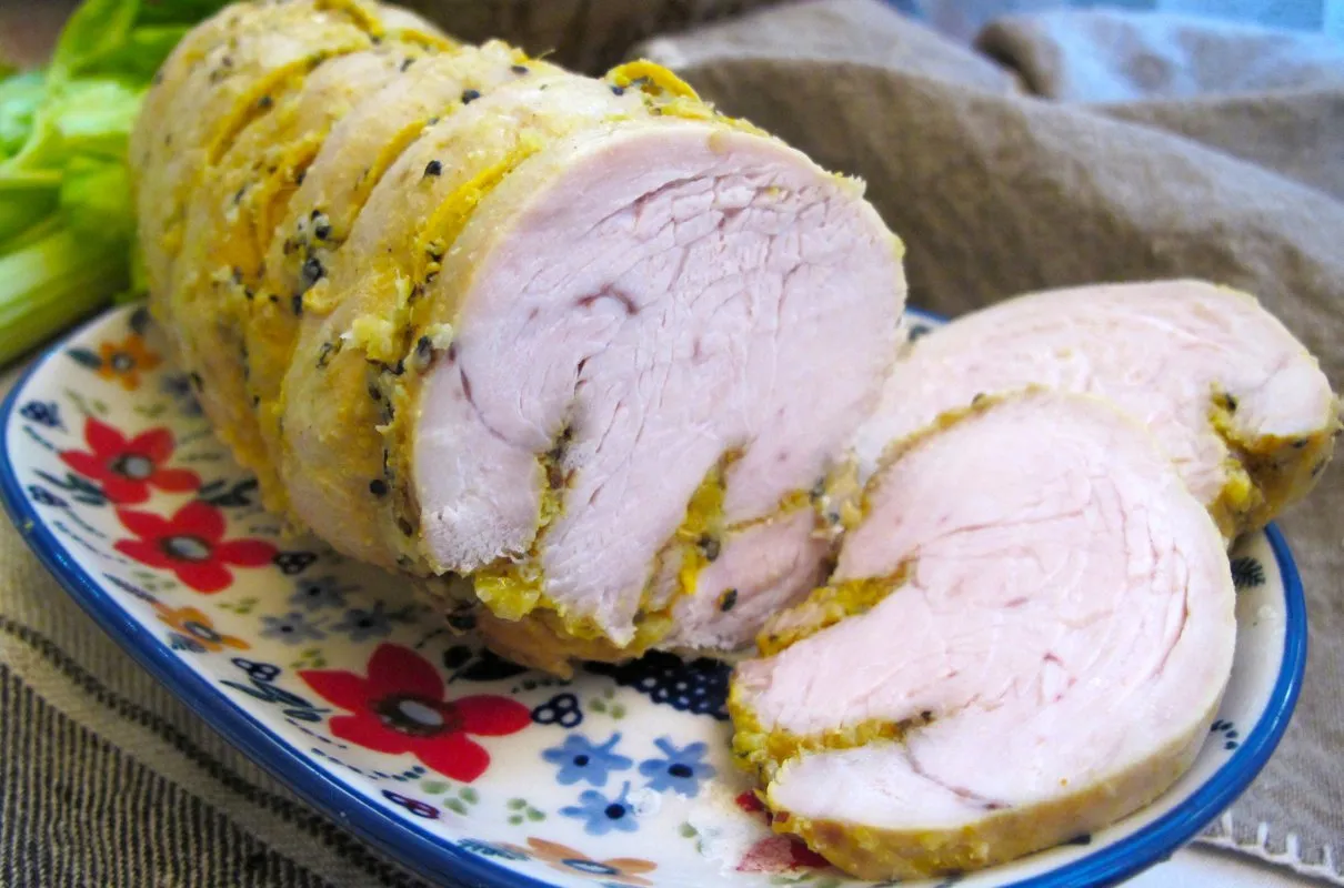 Soczysta pierś z indyka w sosie, pokrojona w plastry, na talerzu z kwiatowym wzorem. Idealna inspiracja, jak zrobić pierś z indyka w sosie.