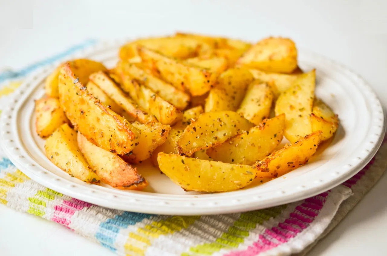 Złociste frytki z piekarnika, przyprawione ziołami, kuszą na białym talerzu. Lepsze niż ziemniaki z wody!