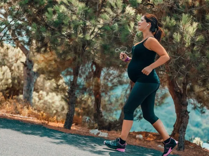 kobieta w ciąży biegnie w parku, uśmiechnięta, bezpieczne bieganie w ciąży