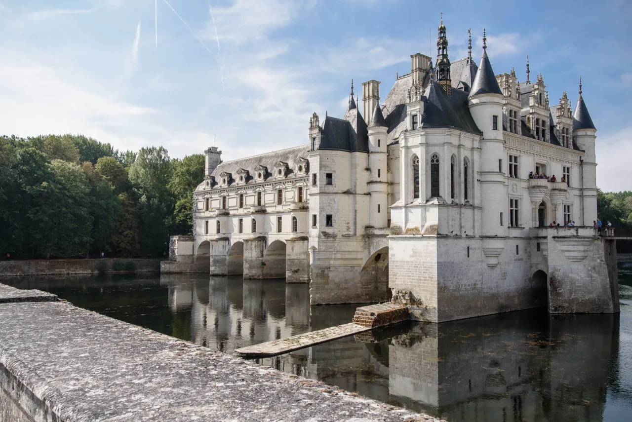 Majestatyczny zamek na wodzie we Francji, z odbiciem w spokojnej rzece.