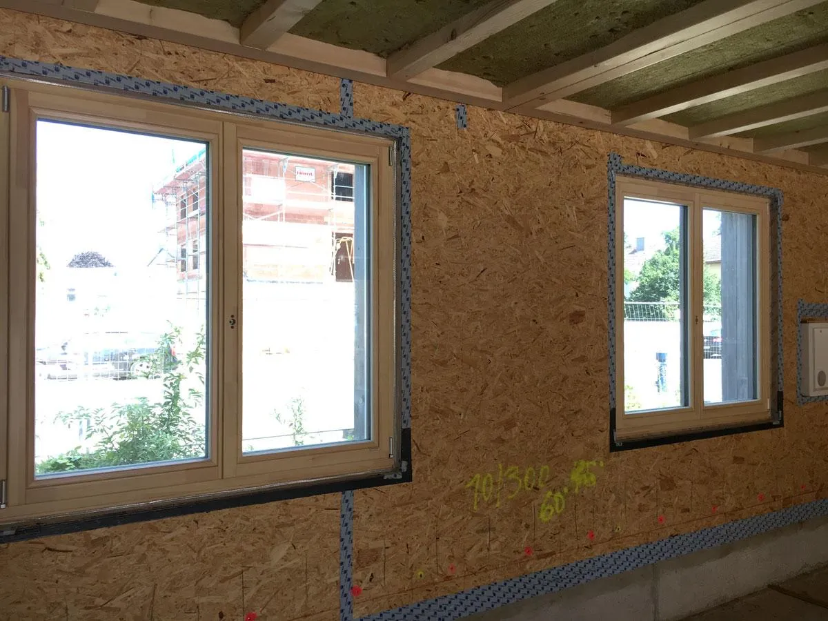 Okna na budowie zabezpieczone taśmą. Widać konstrukcję dachu i ściany z płyt OSB.