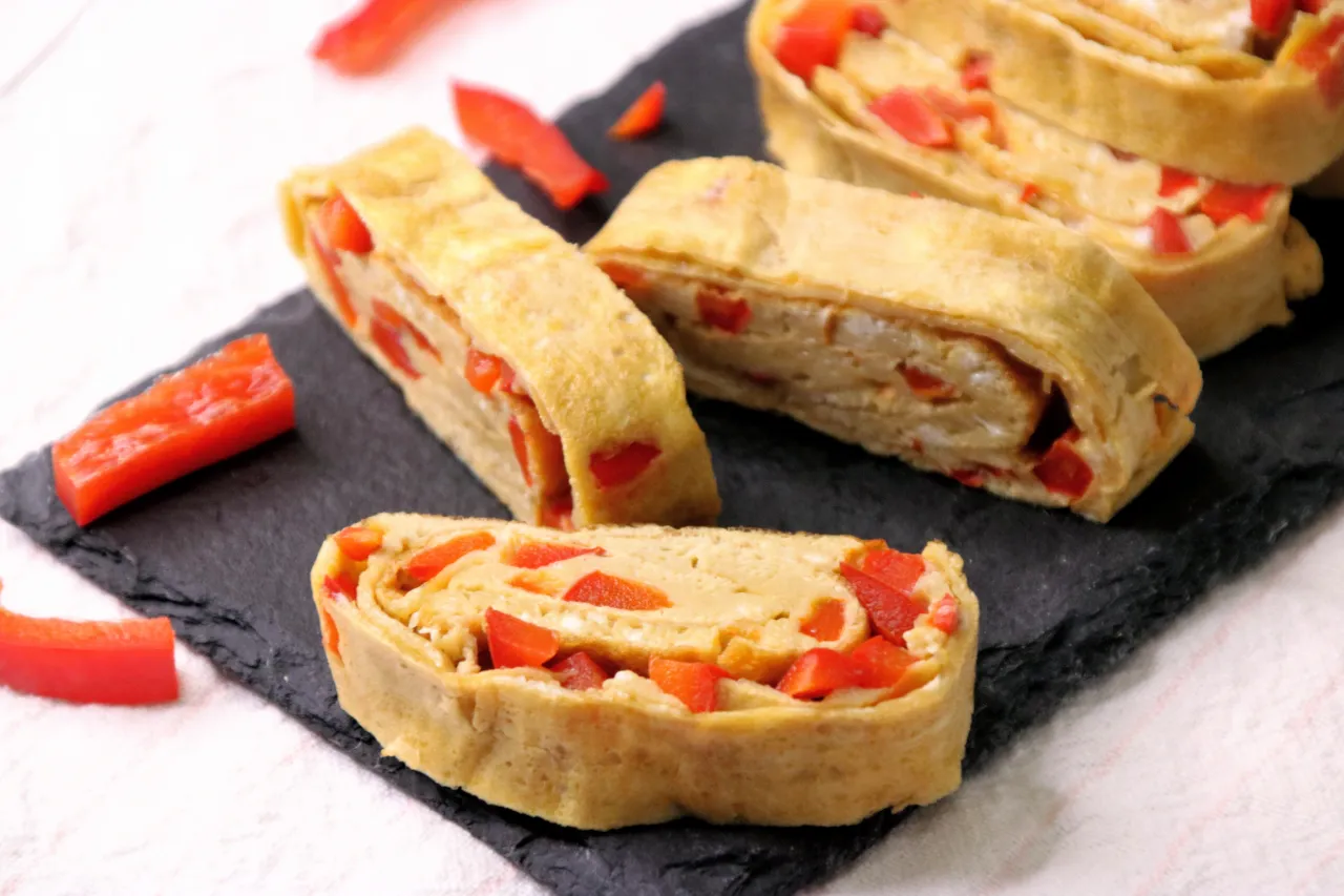 Roladki omlet tamago z papryką, podane na czarnej desce.