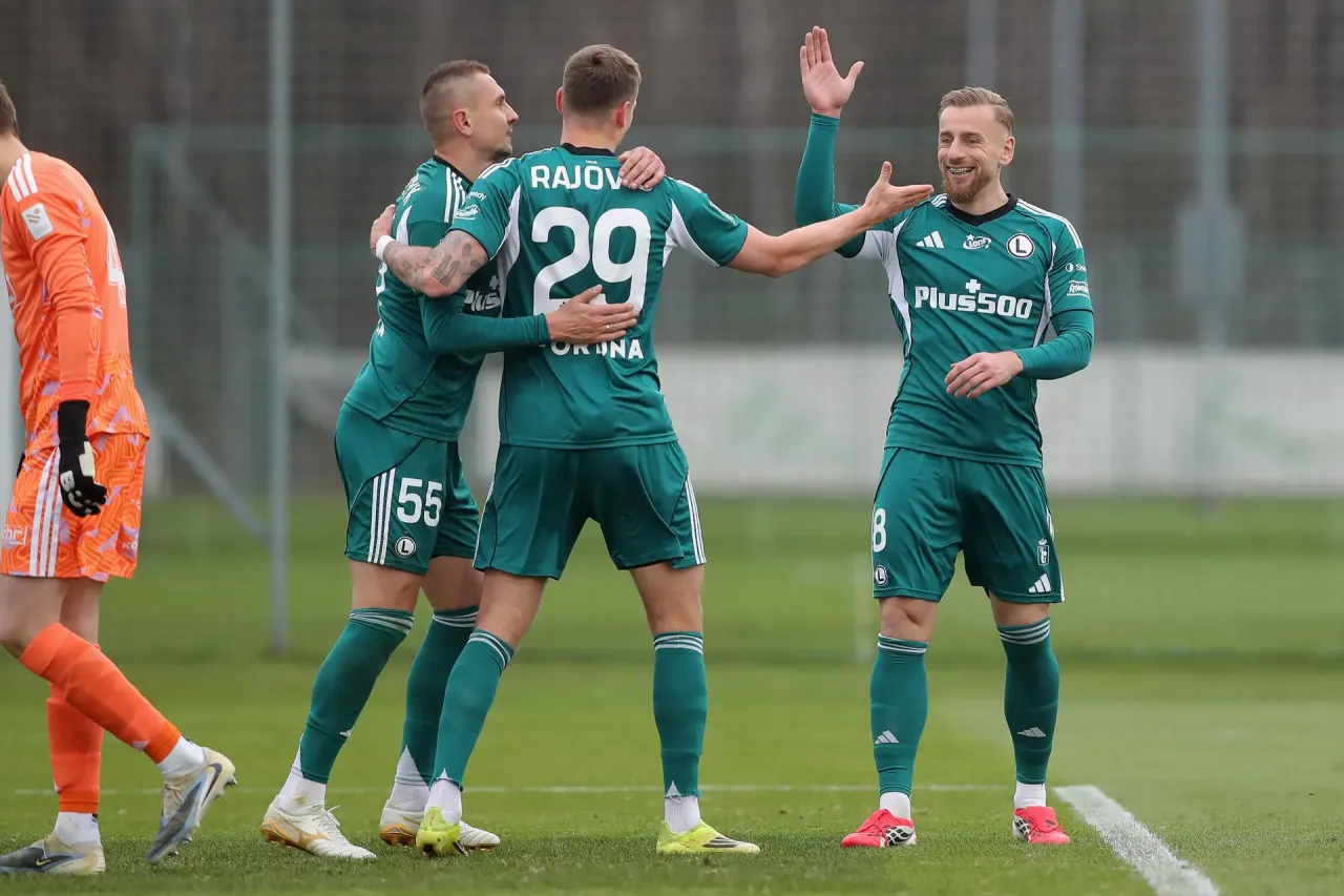 Trzech zawodników Legii Warszawa świętuje bramkę. Jeden z nich, z numerem 29 na plecach, jest obejmowany przez kolegów.