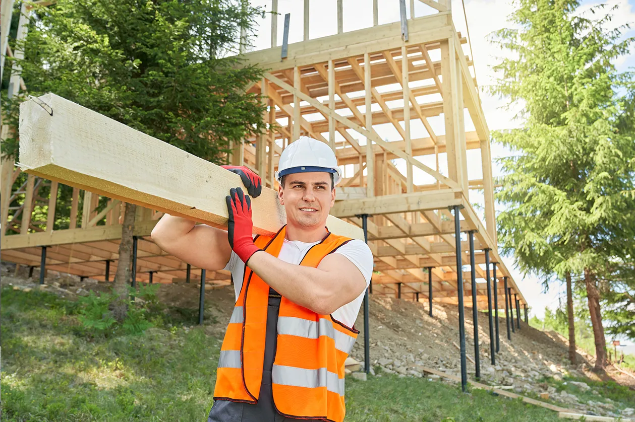 Budowniczy niesie drewno na budowie domu szkieletowego. Czy dom szkieletowy jest tańszy od murowanego?