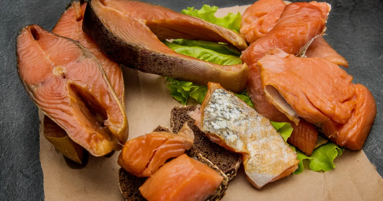 Kawałki wędzonego łososia na liściach sałaty i ciemnym pieczywie. Czy łosoś wędzony jest zdrowy? Tak, to bogactwo kwas&oacute;w omega-3.